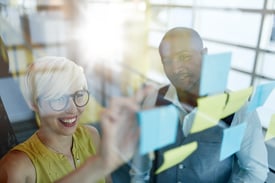 Two creative millenial small business owners working on social media strategy brainstorming using adhesive notes in windows.jpeg